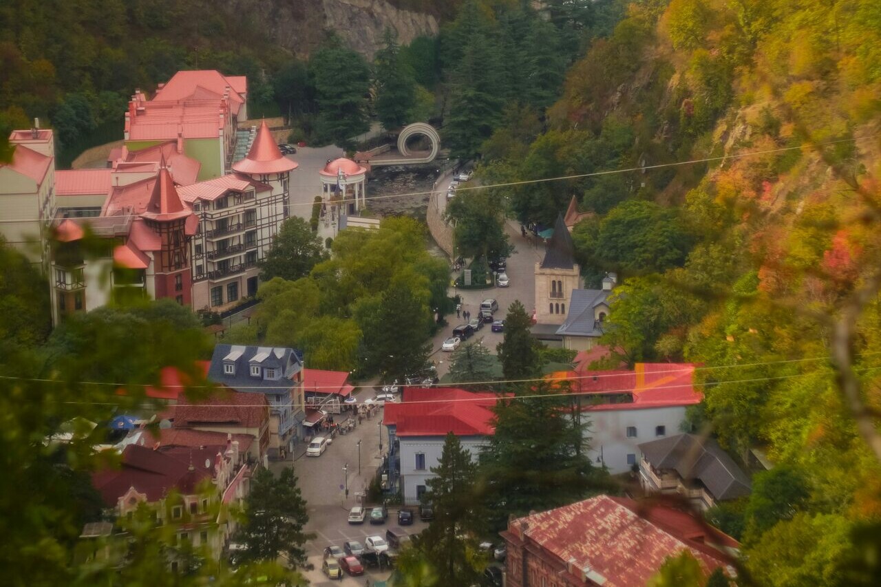 ბორჯომის ხედი მთიდან: ქალაქი მდინარის ხეობაში გადაშლილია, ორივე მხარეს ტყიანი მთები ამოდის.