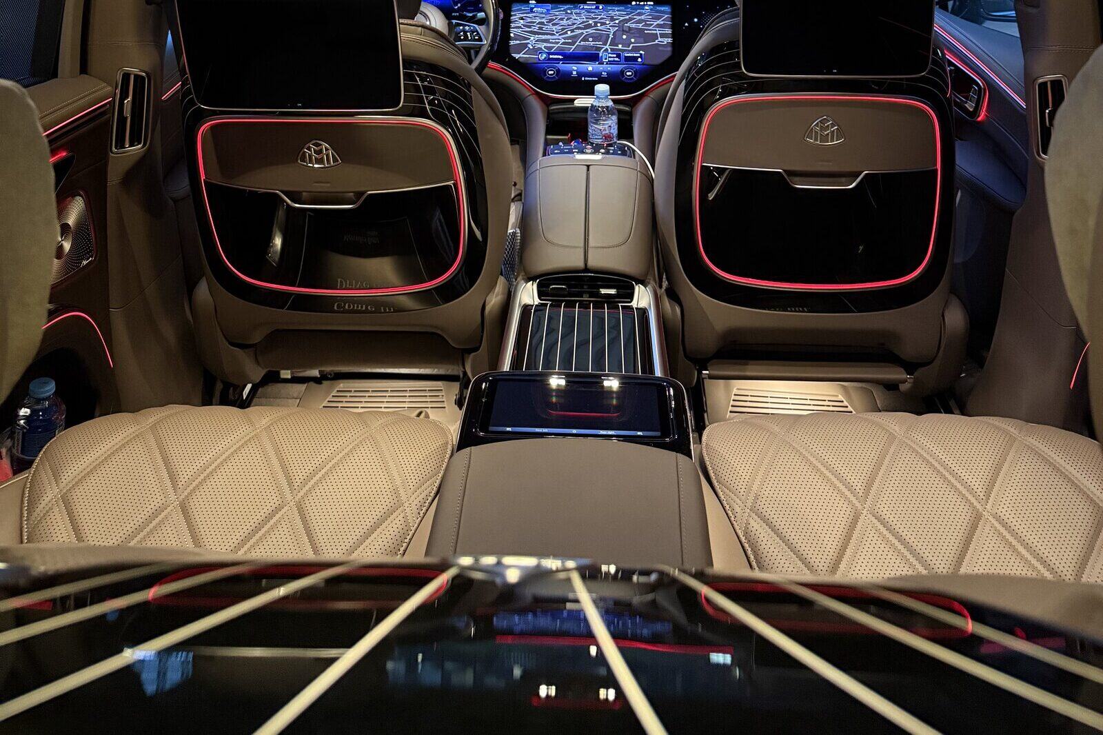 Mercedes-Maybach EQS-ის ორი ნაკერიანი უკანა სავარძელი, უკნიდან; მათ წინ, წინა სავარძლების საზურგეებზე, ეკრანებია.