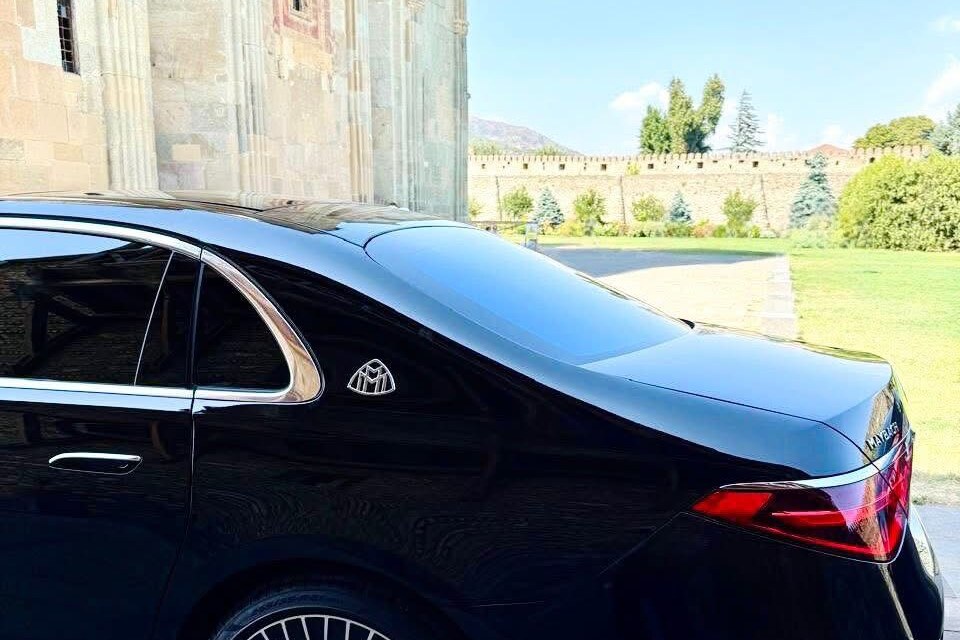 SOIT-ის შავი Mercedes-Maybach S-Class უკნიდან, მცხეთაში, სვეტიცხოვლის ტაძრის ქვის კედლის გვერდით; უკან ძველი ციხის გალავანი და გაზონი.