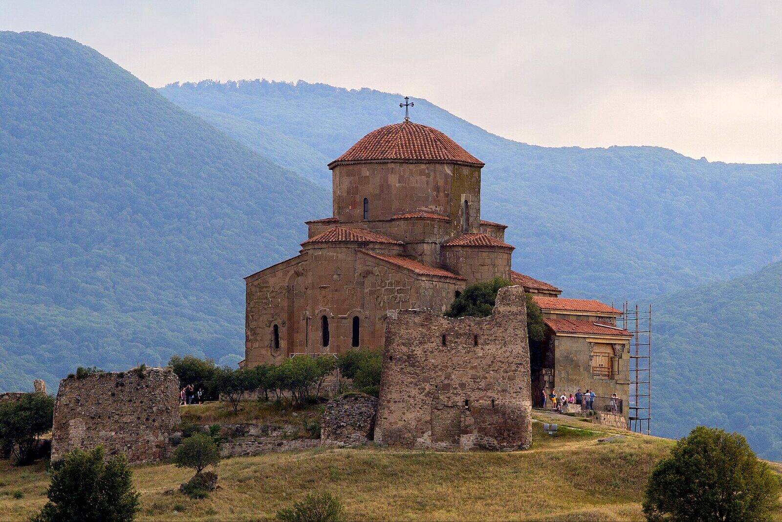 ჯვრის მონასტრის გუმბათოვანი ქვის ეკლესია მცხეთის თავზე, მთის წვერზე, ტყიანი მთების ფონზე.
