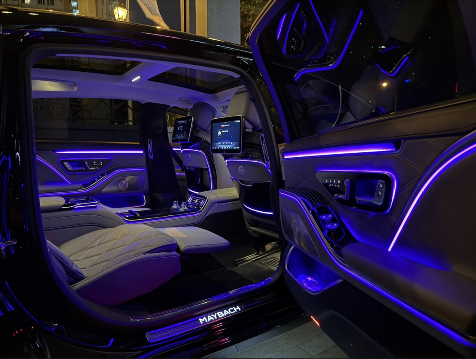 SOIT-ის Maybach უკანა კარის გახსნით ღამის მისვლისას, თბილად განათებული სალონი თბილისის სასტუმროს ბნელი ფასადის ფონზე.
