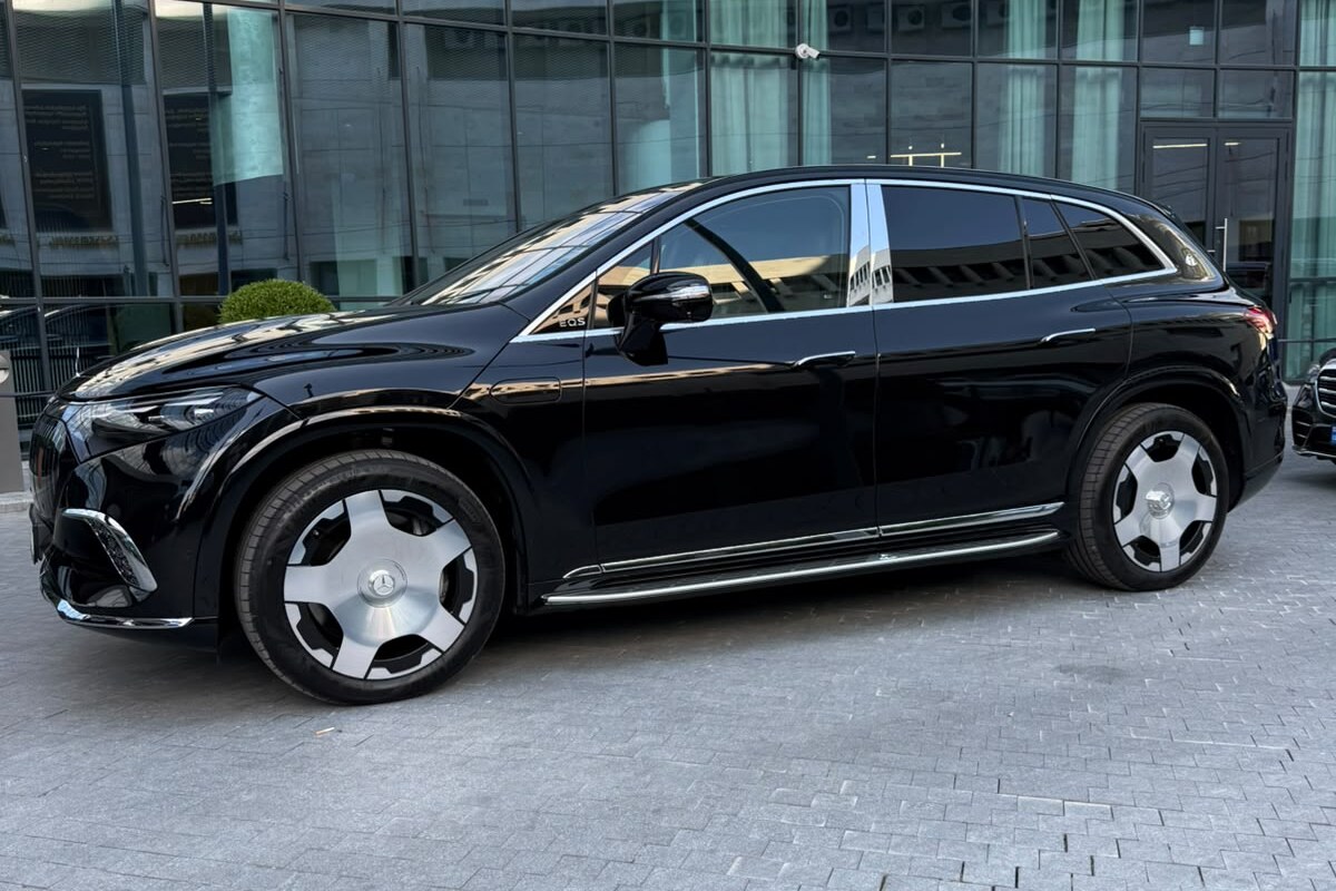 შავი Mercedes-Maybach EQS 680 გვერდიდან, შუშის ფასადის მქონე შენობის წინ, თბილისში.