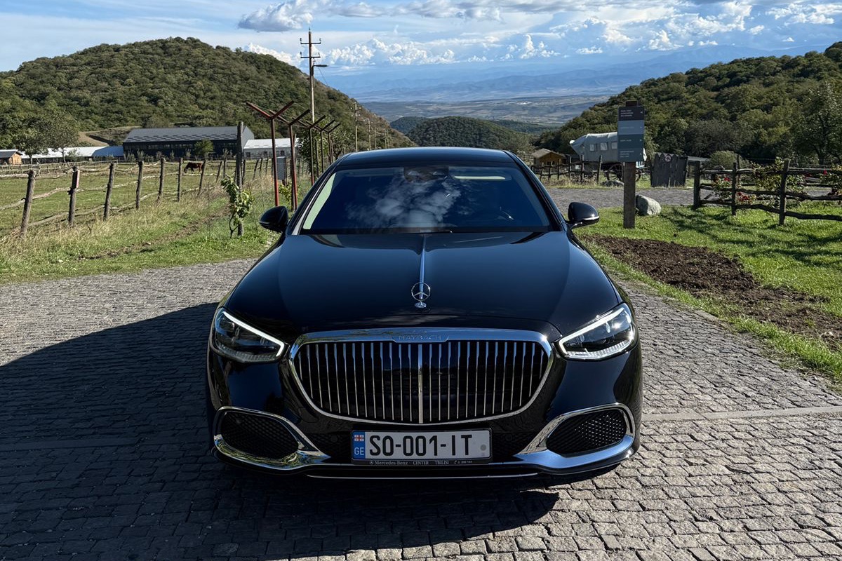 შავი Mercedes-Maybach S-Class კახეთის გორაკებში მარნის შესასვლელთან, ალაზნის ველი ღობის უკან გადაშლილი.
