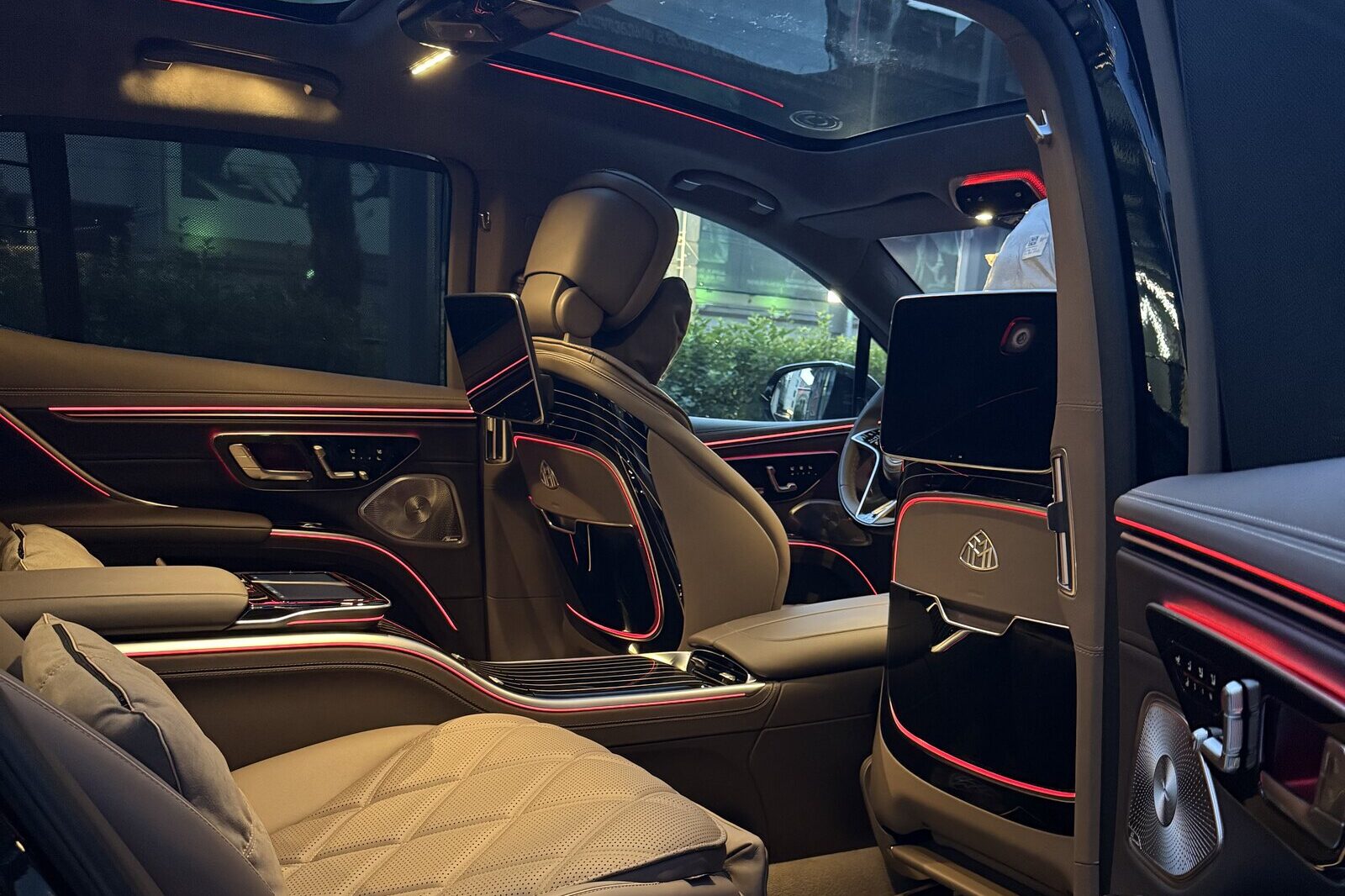 Mercedes-Maybach EQS-ის უკანა სალონი მარჯვენა კარიდან: ნაკერიანი სავარძლები, ცენტრალური კონსოლი და შორს წინა სალონი.