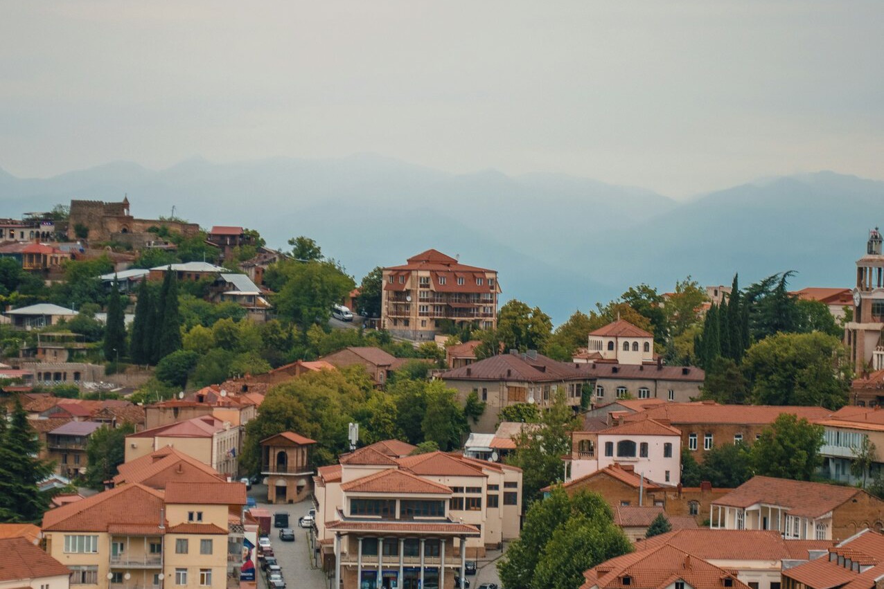 სიღნაღის წითელი კრამიტიანი სახურავები ალაზნის ველისკენ ჩამოდის, კავკასიონის მთები შორს ნისლში.