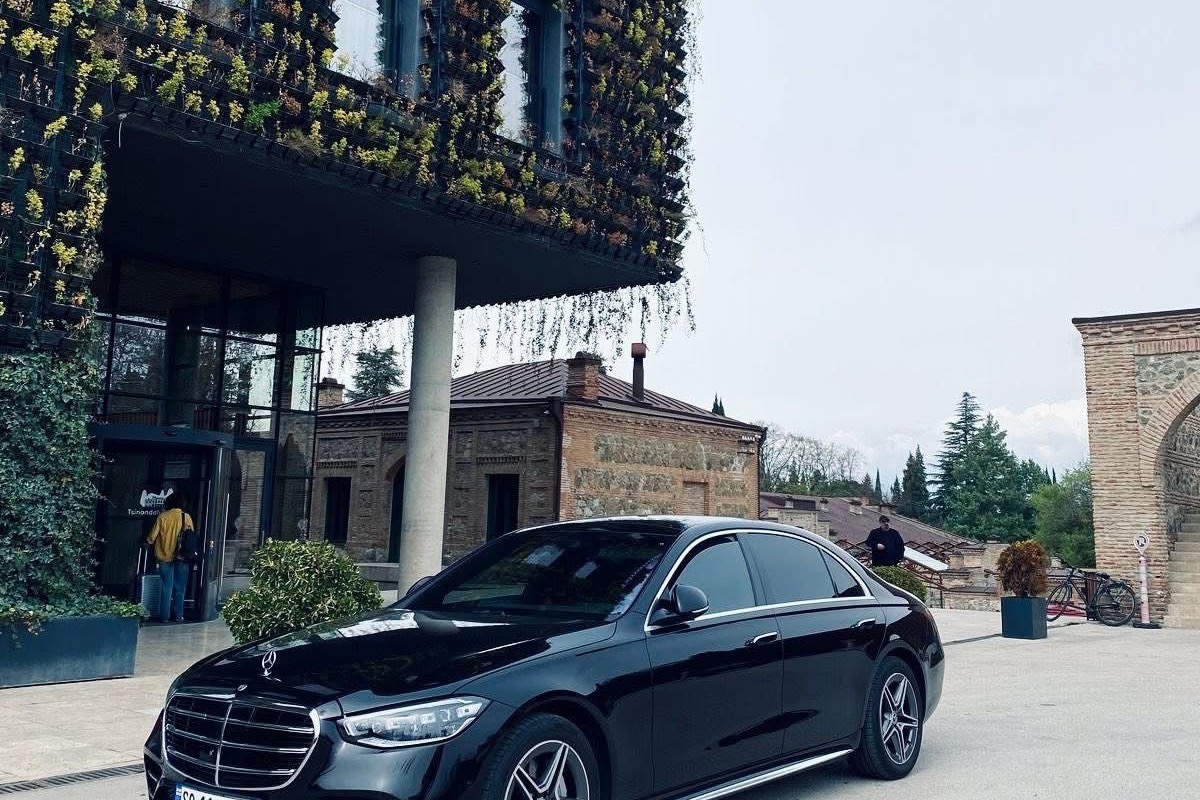 შავი Mercedes-Benz S-Class სასტუმრო Stamba-ს შესასვლელთან თბილისში, შენობის ვერტიკალური ბაღის ფასადი მის უკან.