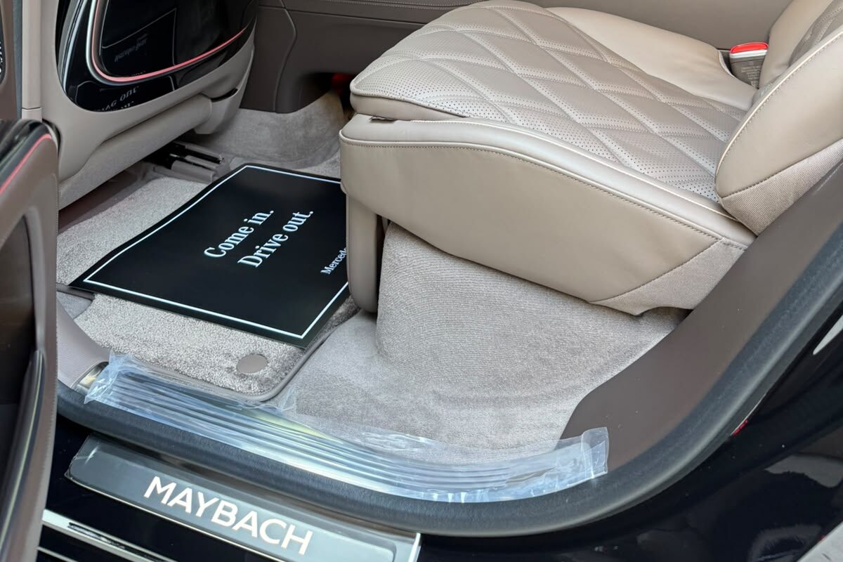 Mercedes-Maybach EQS-ის უკანა სალონის იატაკი: ნაკერიანი სავარძლის ქვედა ნაწილი, ხალიჩა და MAYBACH ზღურბლი.