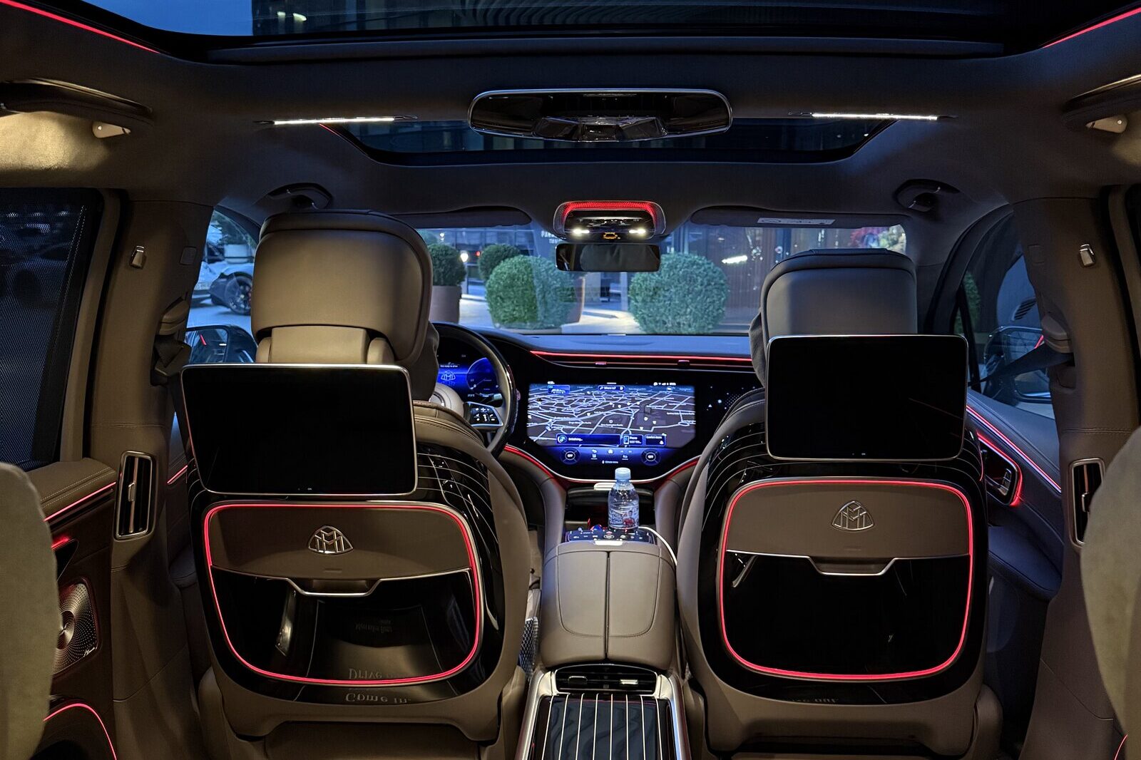 Mercedes-Maybach EQS-ის უკანა სალონი, ხედი წინ: ეკრანები წინა სავარძლების საზურგეებზე, ცენტრალური კონსოლი და წინა პანელის დისპლეი.