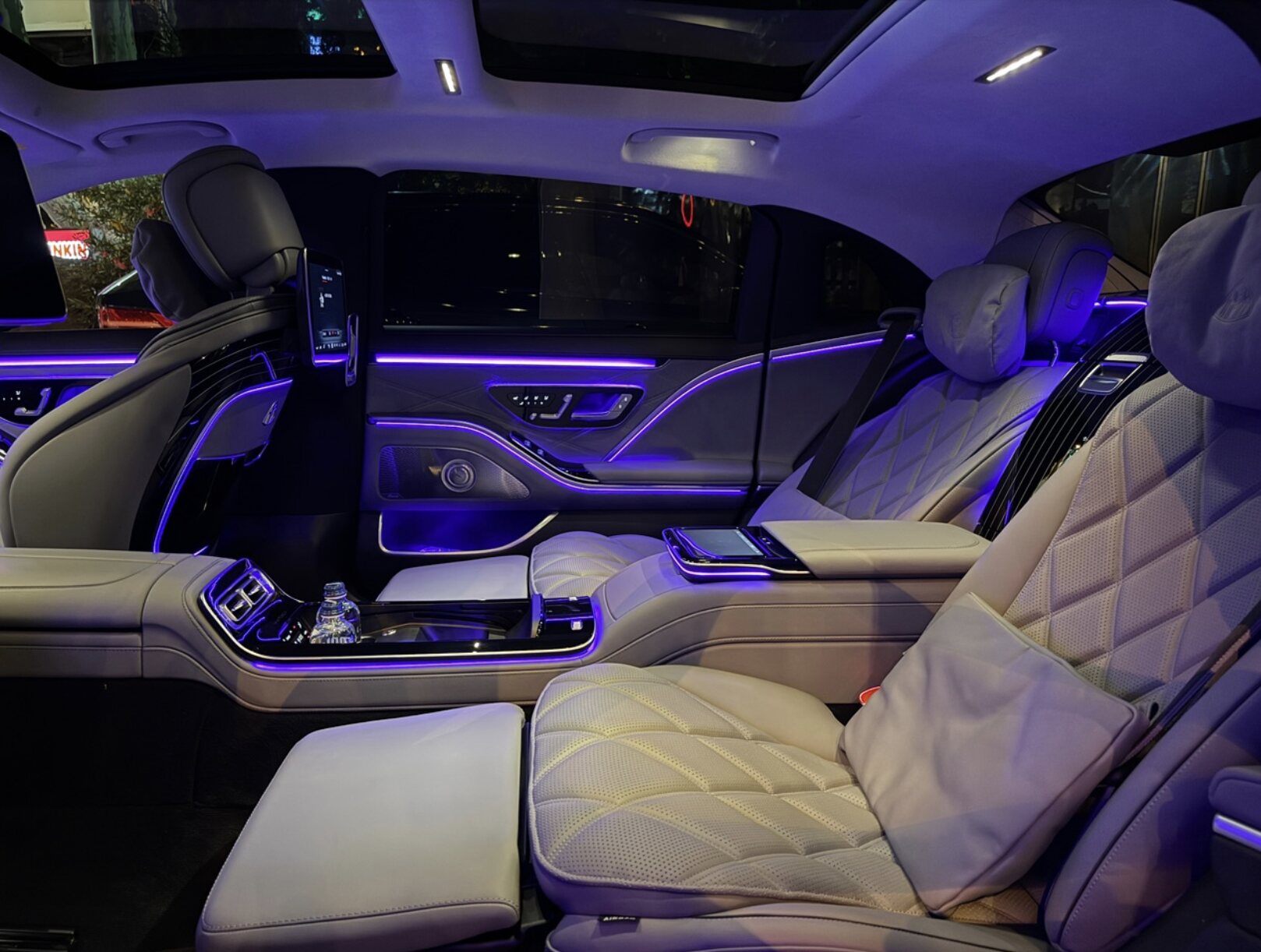 Mercedes-Maybach-ის უკანა სალონის ინტერიერი: კრემისფერი ტყავი რომბული ნაკერებით, იისფერი ფონის განათება, ცენტრალური კონსოლი.